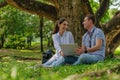 Two young business people sitting together under tree working with laptop computer together in park Royalty Free Stock Photo