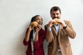 Two young business people or smart casual white man and African American woman holding eating fat tasty American hamburger burger Royalty Free Stock Photo