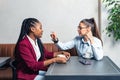 Two young business woman colleagues taking a break in nearby cafeteria drinking coffee talking about private life, to get know Royalty Free Stock Photo