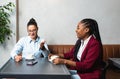 Two young business woman colleagues taking a break in nearby cafeteria drinking coffee talking about private life, to get know Royalty Free Stock Photo