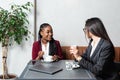 Two young business woman colleagues taking a break in nearby cafeteria drinking coffee talking about private life, to get know Royalty Free Stock Photo