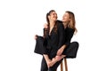 Two young business woman dressed black suit laugh and happy. One woman sitting chair and hugging other woman with barefoot legs Royalty Free Stock Photo