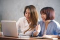 Two young business women sitting at table in cafe. Asian women using laptop and cup of coffee. Freelancer working in coffee shop. Royalty Free Stock Photo