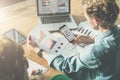 Two young business women sitting at table.First woman signs documents,second holds graph and using smartphone. Royalty Free Stock Photo