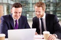 Two young businessmen having coffee, using a laptop computer