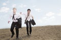 Two young businessmen running and exhausted in the desert, holding jackets