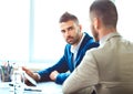 Two young businessmen using touchpad at meeting