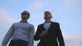 Two young businessmen walking in city with blue sky at background. Business men commuting to work together. Confident Royalty Free Stock Photo