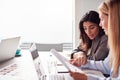 Two Young Businesswomen In Meeting Around Table In Modern Workspace Discussing Documents