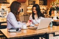 Two young businesswomen sitting in cafe at table and using laptop, working, blogging. Royalty Free Stock Photo