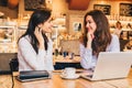 Two young businesswomen sitting in cafe at table and using laptop, working, blogging. Royalty Free Stock Photo