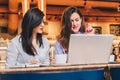 Two young businesswomen sitting in cafe at table and using laptop, working, blogging. Girls are looking at monitor Royalty Free Stock Photo