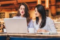 Two young businesswomen sitting in cafe at table and using laptop, working, blogging. Girls are looking at monitor Royalty Free Stock Photo