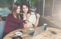 Two young businesswomen are sitting in cafe at table,working together, girl is pointing at laptop screen. Royalty Free Stock Photo