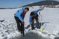 Two young Caucasian man looking at a hole on an ice on a frozen lake with saw and ice drill auger