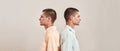 Two young caucasian men, twin brothers standing back to back  over beige background Royalty Free Stock Photo