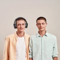 Two young caucasian twin brothers in casual wear listening music in headphones and wireless earphones, while standing Royalty Free Stock Photo