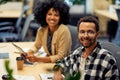 Two young cheerful male and female office workers sitting at desk , smiling at camera while working together in Royalty Free Stock Photo