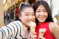 Two young Chinese girls taking a selfie while eating an ice cream cone in the typical streets of Granada