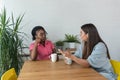 Two young colleagues at a web developing company a black and a white woman sitting down for a coffee break and talk Royalty Free Stock Photo