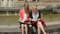 Two young college coeds learn together sitting by the fountain in the park. The sun is shining.