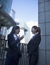 Two young confident businesswomen talking outdoors in Beijing, with CCTV building in the background