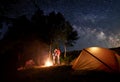 Two young couples at campfire under bright starry sky near tent on background of trees