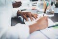 Two young coworkers working together in a modern office and making notes on documents.Closeup of pen holding in