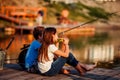 Two young cute little friends, boy and girl eating sandwiches and fishing on a lake in a sunny summer day Royalty Free Stock Photo