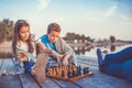 Two young cute little friends, boy and girl having fun while playing chess sitting by the lake in the evening Royalty Free Stock Photo