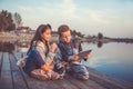 Two young cute little friends, boy and girl having fun watching some interesting video on the tablet while sitting by the lake Royalty Free Stock Photo