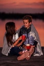 Two young cute little friends, boy and girl talking while sitting covered with blanket during sunset Royalty Free Stock Photo