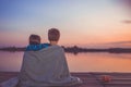 Two young cute little friends, boy and girl talking while sitting hugging and covered with blanket by the lake during sunset Royalty Free Stock Photo