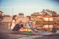 Two young cute little friends spending great time by the lake, while eating sandwiches, drinking tea talking and fishing on a lake Royalty Free Stock Photo