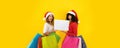 Two young cute women wearing Santa Claus hat looking to the camera with astonished face, open mouth, wide eyes, holding colored Royalty Free Stock Photo