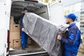 Two Delivery Men Unloading Furniture From Vehicle