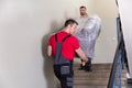 Two Young Delivery Men In Uniform Unloading Furniture