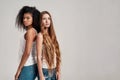 Two young diverse women wearing white shirts looking at camera while standing together isolated over grey background Royalty Free Stock Photo