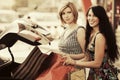 Two young fashion women with shopping bags on the car parking