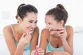 Two young female friends applying makeup in bed