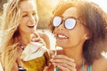 Laughing female friends sipping from coconuts on a sandy beach