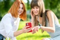 Two young female friends sitting on a bench in summer park taking a selfie by smartphone camera Royalty Free Stock Photo