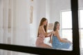 Two young female friends wearing pajamas hairstyling while spending time at home