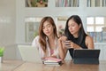 Two young female students with coffee are using a laptop to study online at home in the summer semester