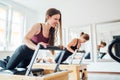 Two young females doing ABS muscles strength exercises using pilates reformer machine in sport athletic gym hall. Active people Royalty Free Stock Photo