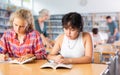 Two young friendly female pupils talking, reading books and making notes