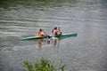 Two young girl athletes in life jackets are sailing canoe on river, controlling oars. Active outdoor sports training. Back view.