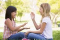 Two young girl friends sitting outdoors playing