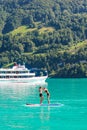 Two young girl friends standing on paddle board on turquoise Lake Brienz in Switzerland. Tourist boat in background. Switzerland