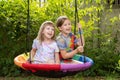 Two young girls, children sitting side by side on a round swing, joyful happy cheerful kids laughing together, sisters siblings, Royalty Free Stock Photo